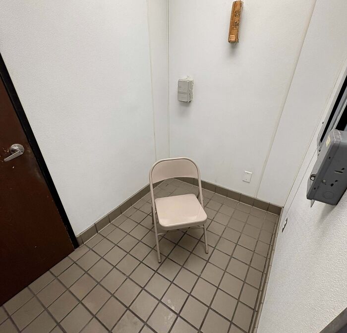 Small, prison-like break room with tiled floor, plain white walls, and a single beige folding chair in the center.