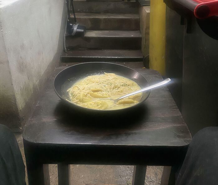 Dull break room resembling a prison cell with a simple meal on a worn wooden table near concrete stairs.
