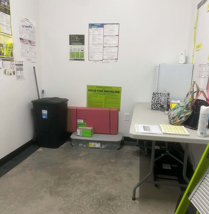Bleak and cramped break room with concrete floors, minimal furniture, and plain white walls resembling a prison environment.
