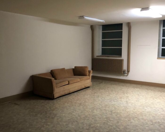 Sparse break room with old brown couch and bars on windows, resembling a prison environment.