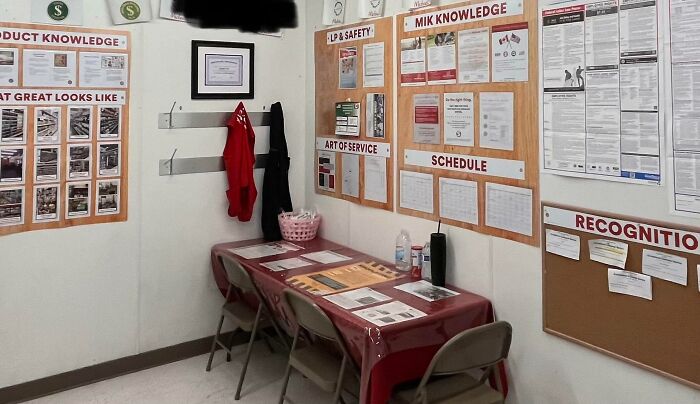 Sparse break room with folding chairs, bulletin boards, and minimal decor, resembling a prison-like environment.