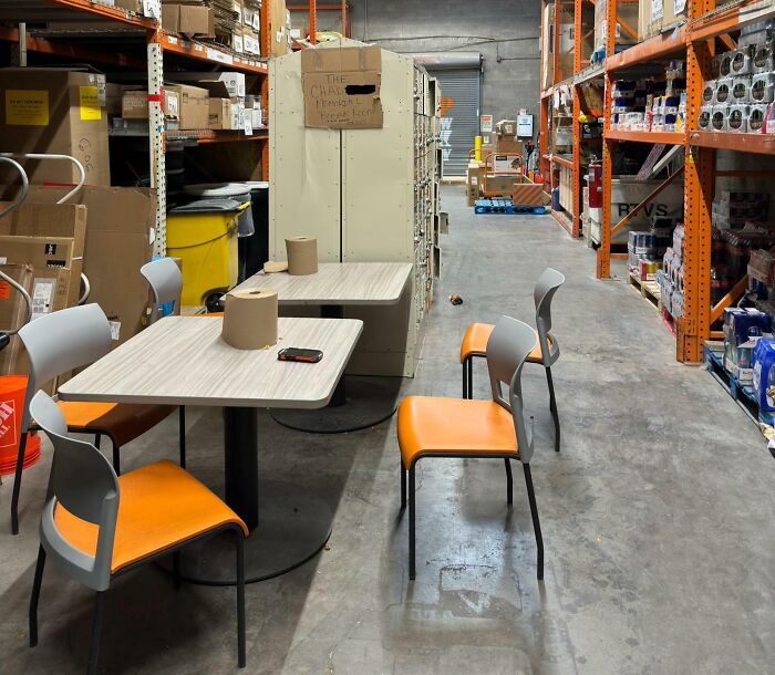 Break room inside a cluttered warehouse with basic tables and chairs, resembling a prison-like atmosphere.