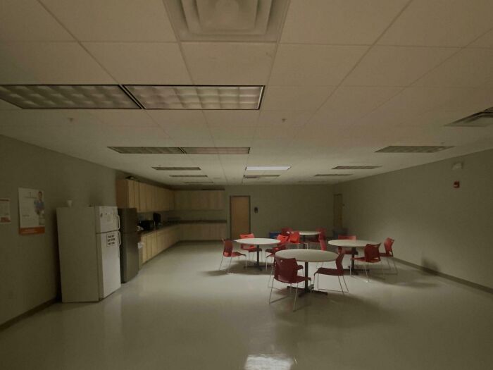 Dim, empty break room with red chairs and round tables, resembling one of the worst break rooms ever.