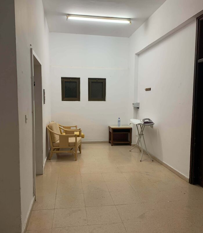 Sparse break room resembling a prison with minimal furniture and harsh fluorescent lighting on bare walls.