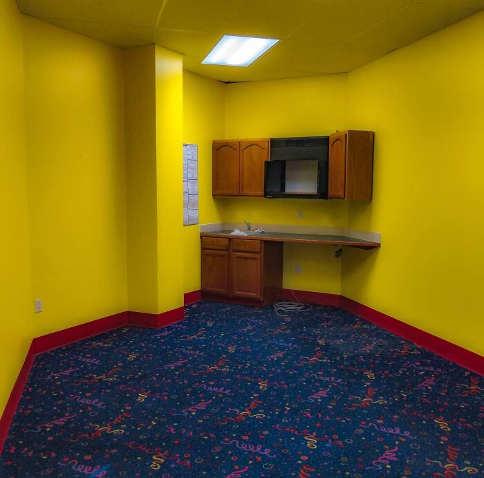 Yellow break room with wooden cabinets and patterned carpet, resembling one of the worst break rooms ever.