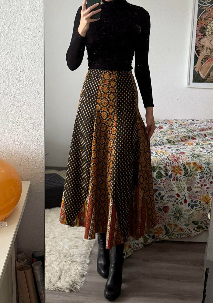 Woman wearing patterned thrift store skirt and black turtleneck, showcasing unique thrift store finds in bedroom mirror.