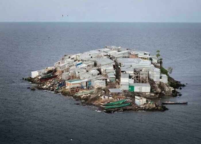 Small overcrowded urban shelter built with makeshift materials on a tiny island surrounded by water depicting urban hell conditions.