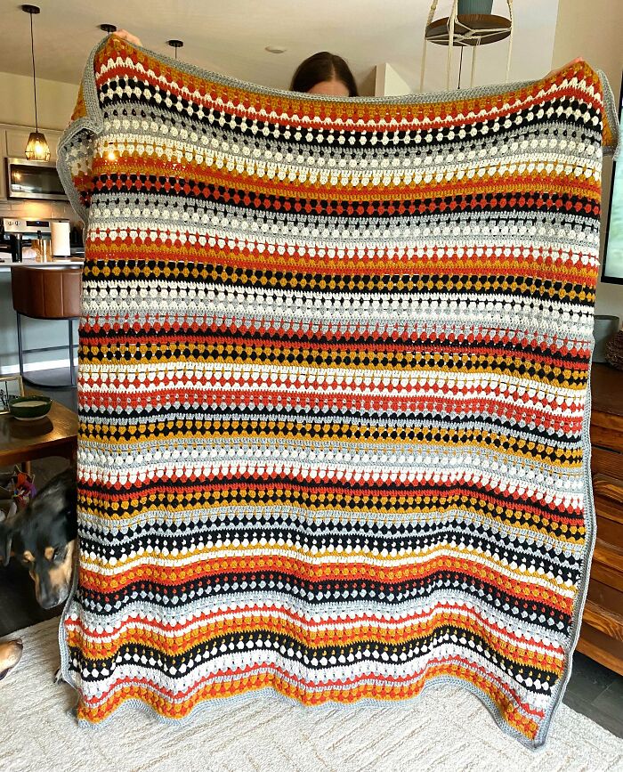Person holding a colorful striped crocheted blanket showcasing the art of crocheting in a cozy home setting.
