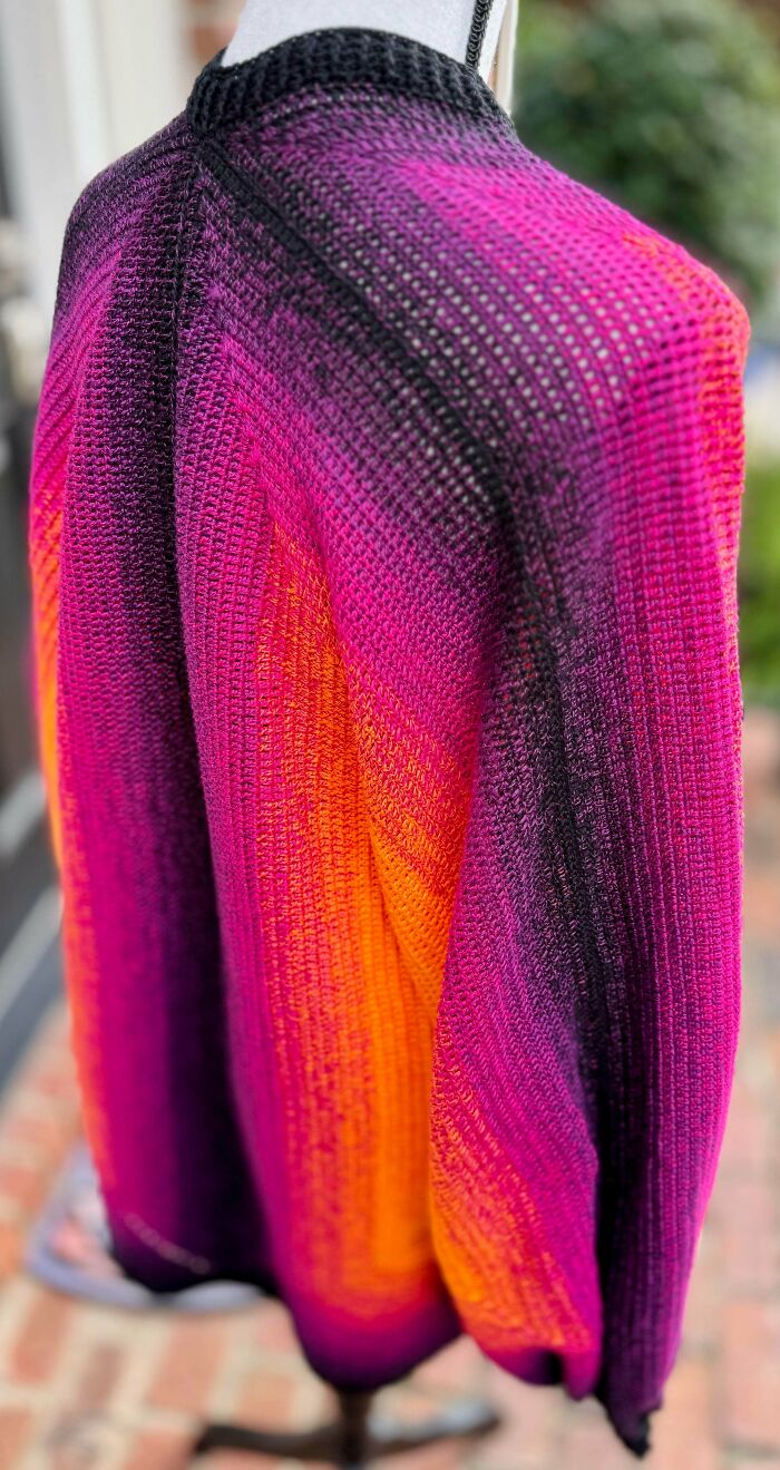 Vibrant crocheted shawl in pink, orange, and black gradient displayed on a white mannequin showcasing crocheting mastery.