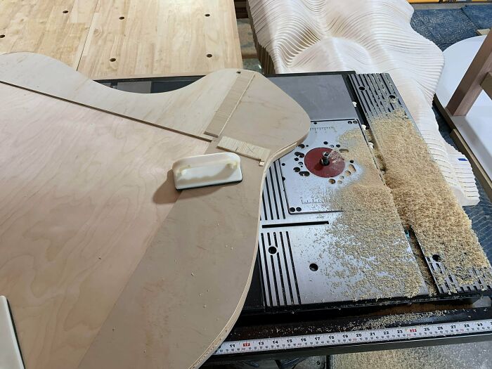 Woodworkers shaping smooth, curved wooden pieces on a workbench surrounded by fine wood shavings.