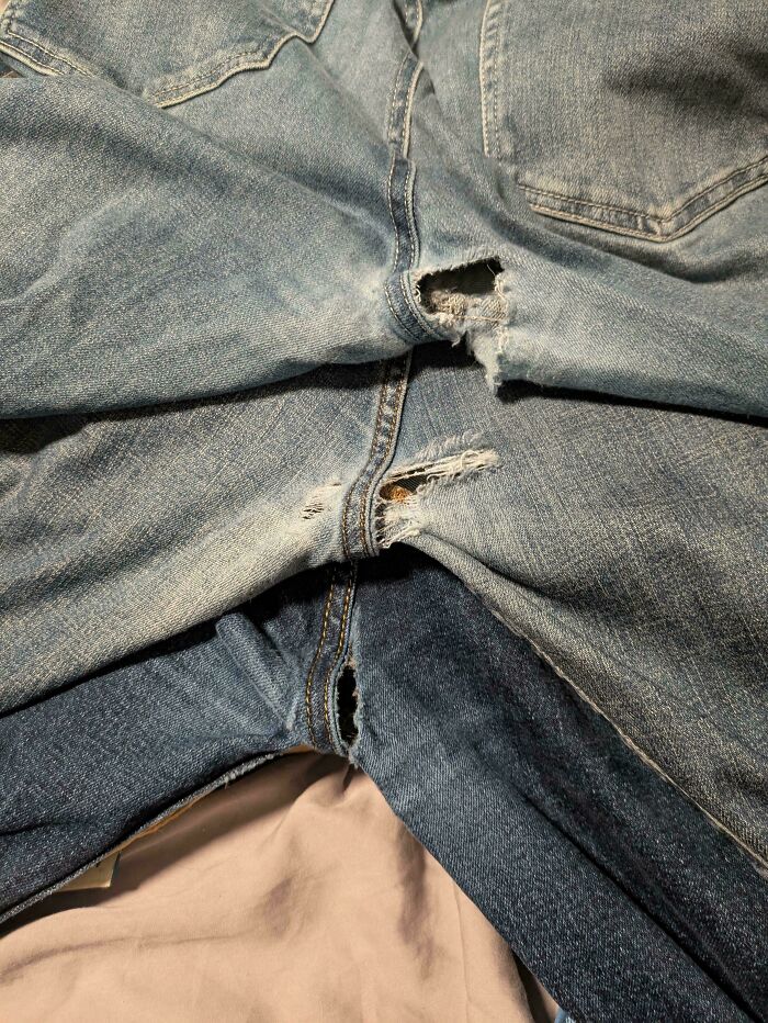 Worn jeans with tears in the c****h area, showing moderately interesting wear patterns and fabric distress.