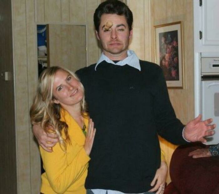 Man with shocked expression and Champagne cork on forehead posing with smiling woman in a perfectly timed photo moment