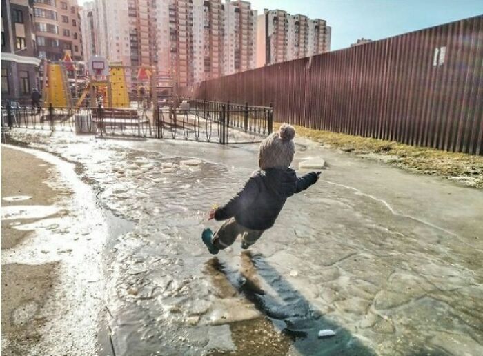 Child slipping perfectly timed mid-fall on icy ground in urban playground, capturing a moment better than Photoshop.