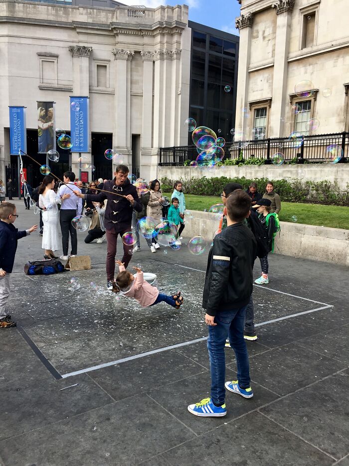 Child appearing to float among soap bubbles in a perfectly timed photo captured outdoors with people watching nearby.