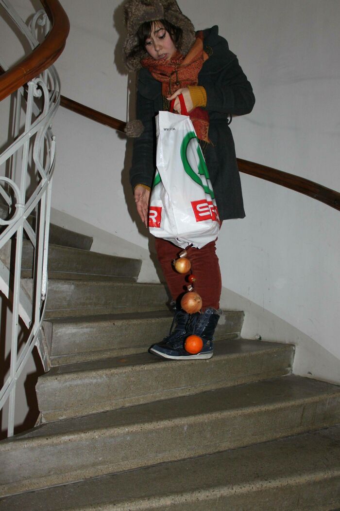 Person wearing winter clothes on stairs with groceries, including onions and an orange, captured in a perfectly timed photo.