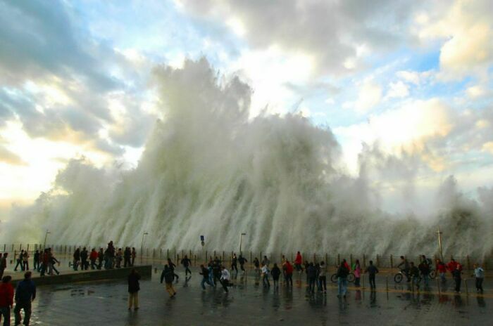 Massive wave crashing over a pier with people scattered, a perfectly timed photo capturing natural power beyond any Photoshop.