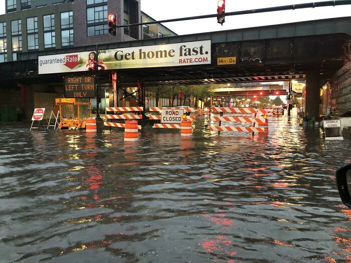 Flooded street with a road closed sign below an ironic advertising placement displaying the phrase Get home fast.