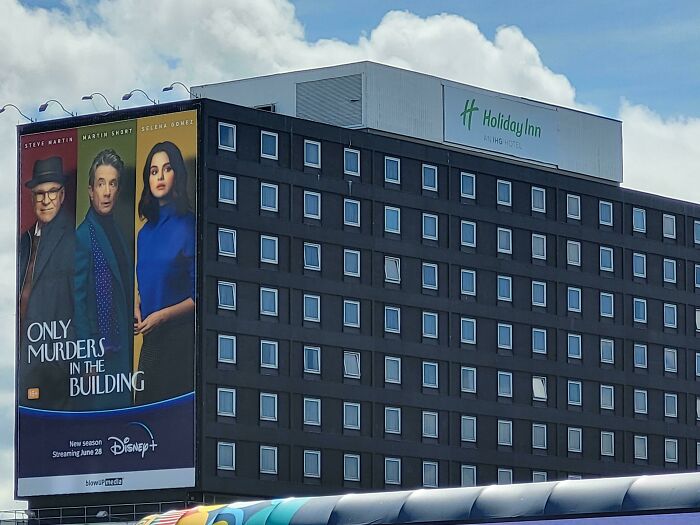 Large building advertisement placement fail showing a vertical Disney+ poster next to a Holiday Inn sign under a blue sky.