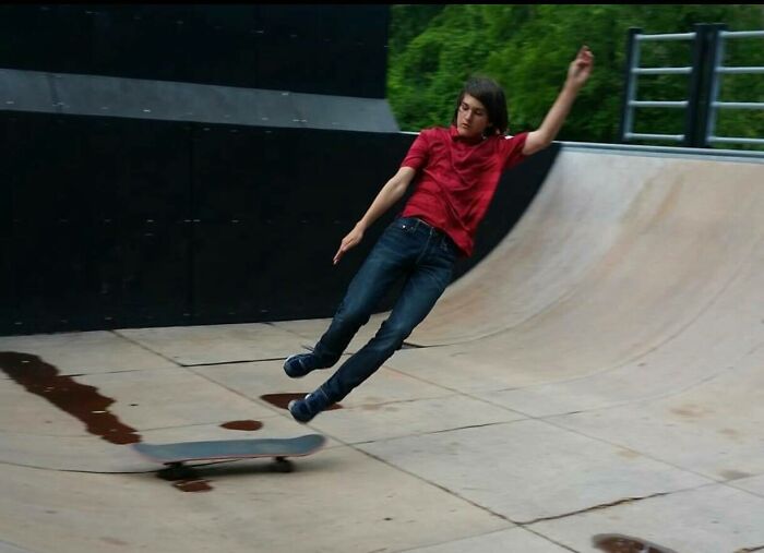 Teenager in a red shirt falling off a skateboard at a skatepark, captured in a perfectly timed photo moment.