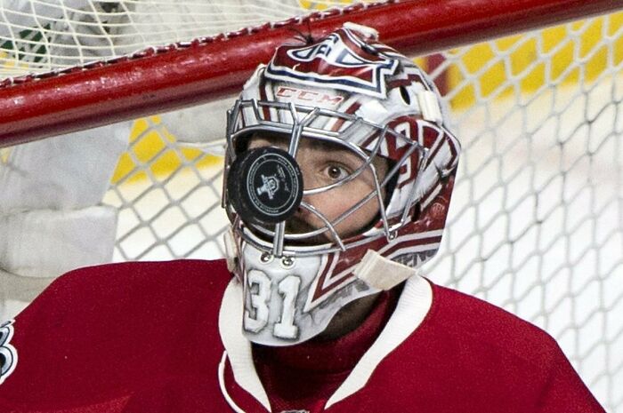 Hockey goalie in red uniform with puck perfectly stuck on face mask during game, a perfectly timed photo moment