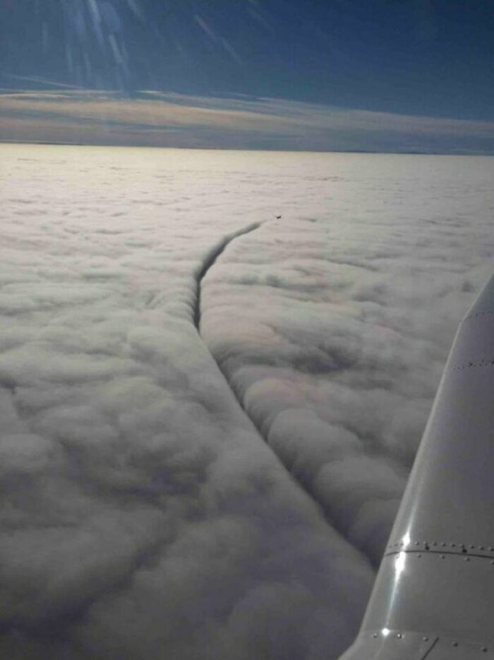 A perfectly timed photo of an airplane wing with a clear trail cutting through thick clouds above the horizon.