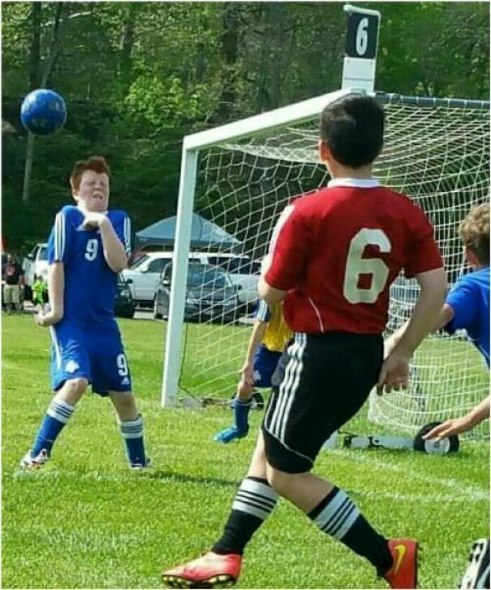 Youth soccer player reacting to a perfectly timed photo capturing a ball about to hit his face in an outdoor match.