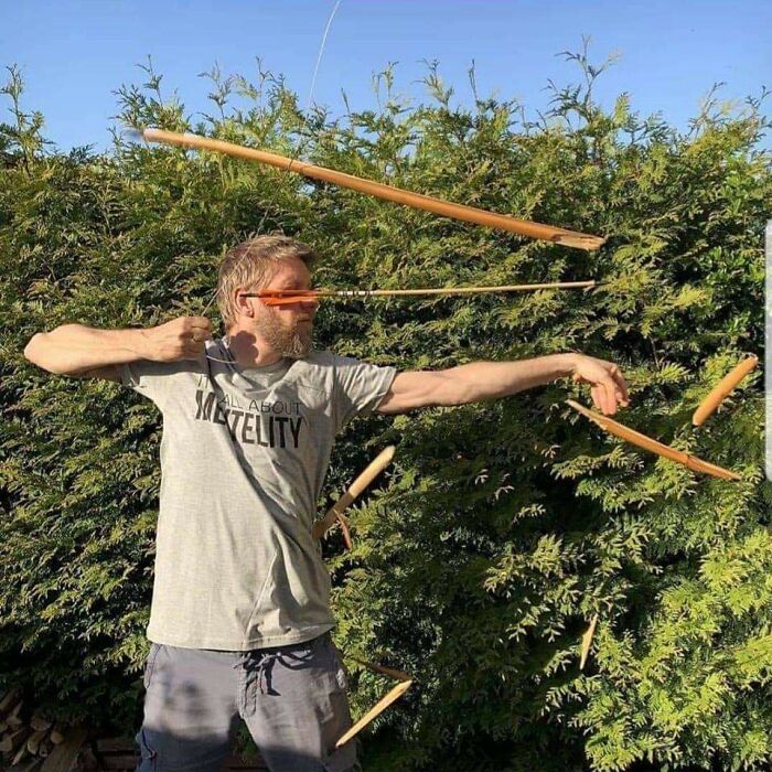 Man aiming a bow and arrow with perfectly timed photo capturing multiple wooden sticks in midair, showcasing perfectly timed photos.