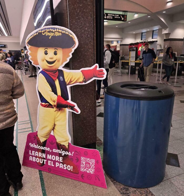 Advertising placement fail showing a mascot cutout awkwardly positioned next to a large trash can indoors.