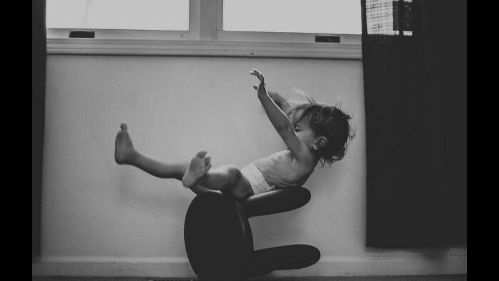 Child captured in a perfectly timed photo falling backwards off a chair, creating a moment better than any Photoshop.