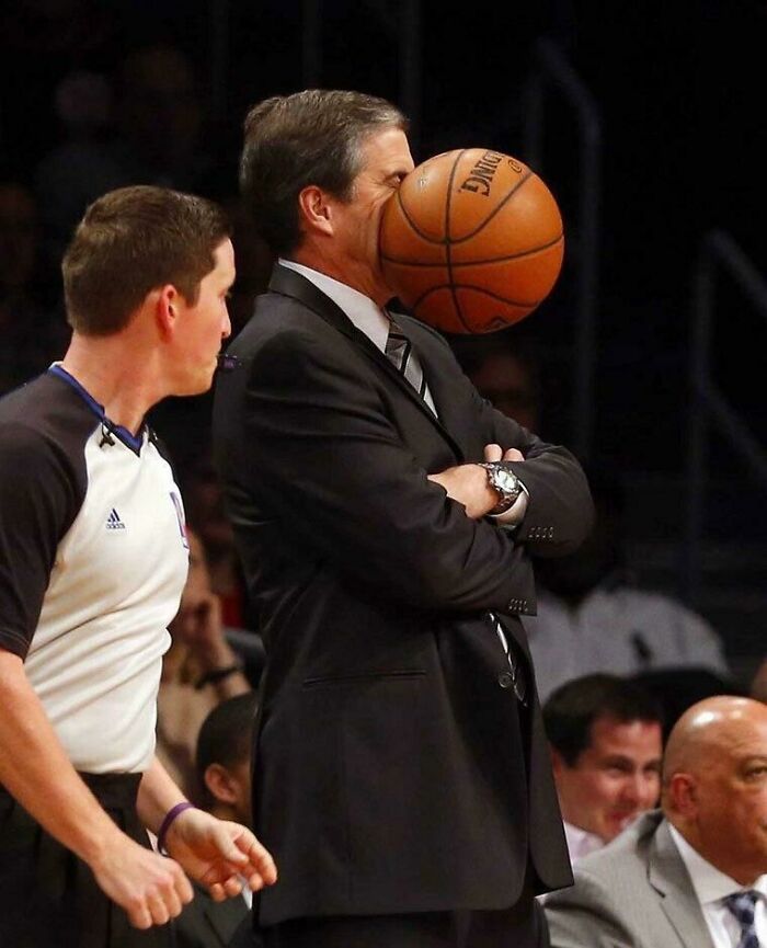 Man in suit getting hit in the face with basketball, perfectly timed photo capturing unexpected moment on court.