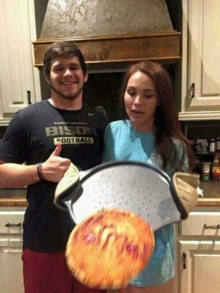 A perfectly timed photo of two people tossing a pizza in the air in a kitchen, capturing motion better than any Photoshop.