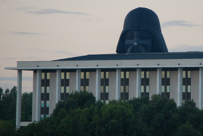 Perfectly timed photo showing a large Darth Vader helmet appearing to sit on top of a building behind trees.