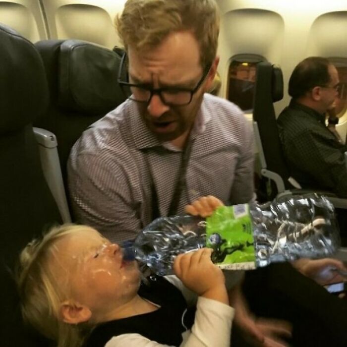 Toddler drinking from an oversized water bottle on an airplane, capturing a perfectly timed photo better than Photoshop.