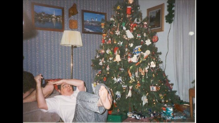 Man falling backward on couch in a living room decorated for Christmas, a perfectly timed photo capturing an unexpected moment.