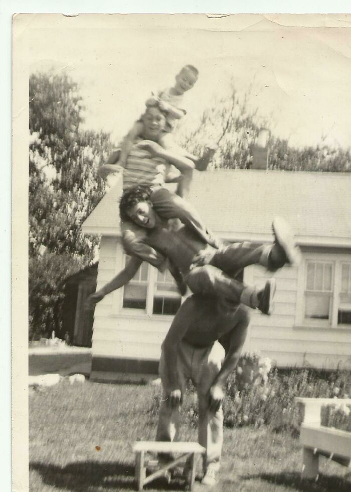 Vintage photo of four people stacked on each other outdoors, showcasing a perfectly timed photo capturing a fun moment.