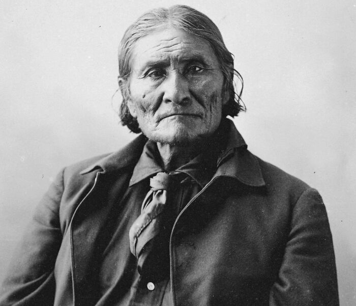 Portrait of an American folk hero with weathered features, wearing a dark coat and scarf, captured in a historic black and white photo.