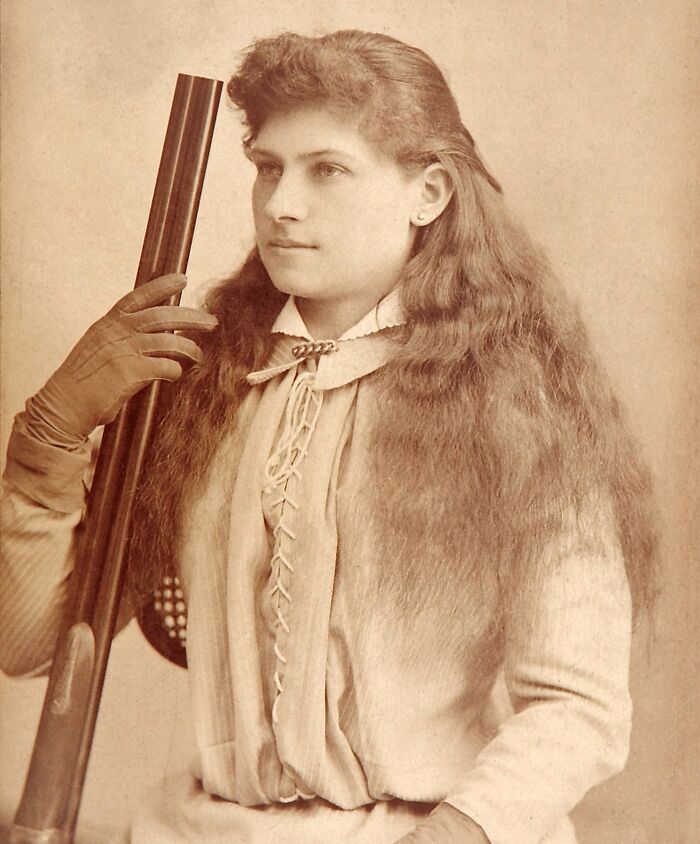 Vintage portrait of a woman American folk hero holding a rifle, wearing gloves and lace-up clothing, symbolizing folk heroes legacy.