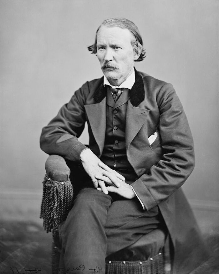 Black and white portrait of an American folk hero seated, dressed in 19th-century formal attire, showing a solemn expression.