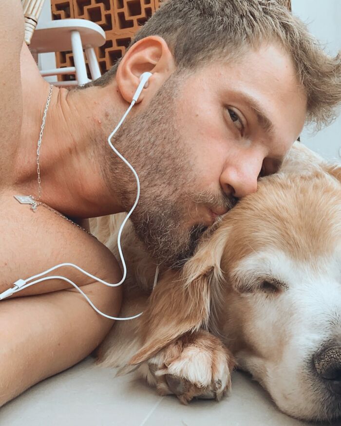 Man wearing earphones lying close and kissing a golden retriever, showing a moment of affection and connection.