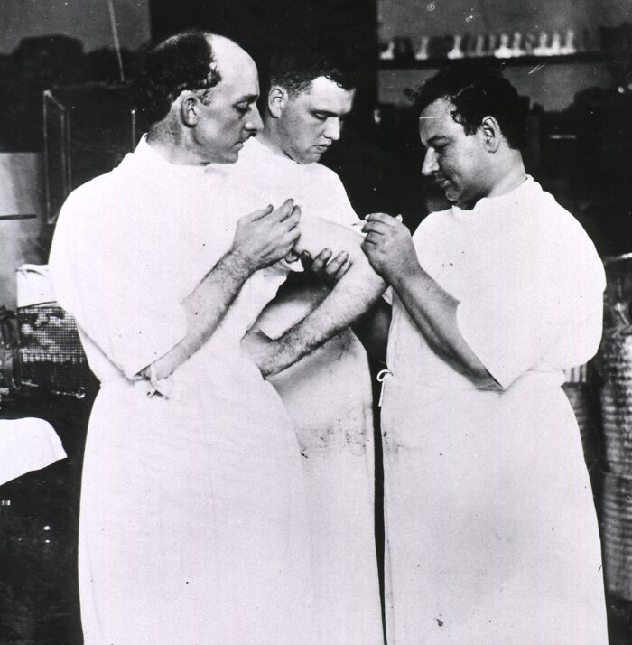 Three medical professionals in old-school medical attire examining and preparing an injection in a vintage clinical setting.