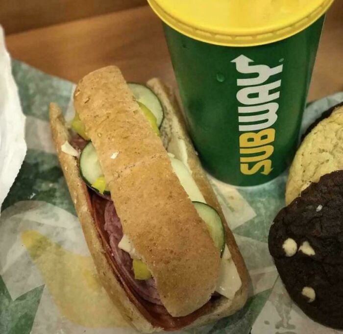 Subway sandwich with pickles, beverage cup, and chocolate chip cookie, evoking '90s posts and nostalgic memories.