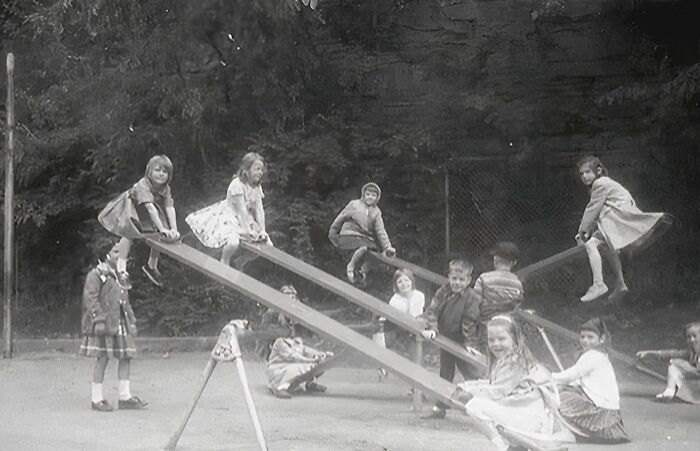 Black and white historic playground photo showing kids playing on seesaws without safety gear, highlighting playground risks.
