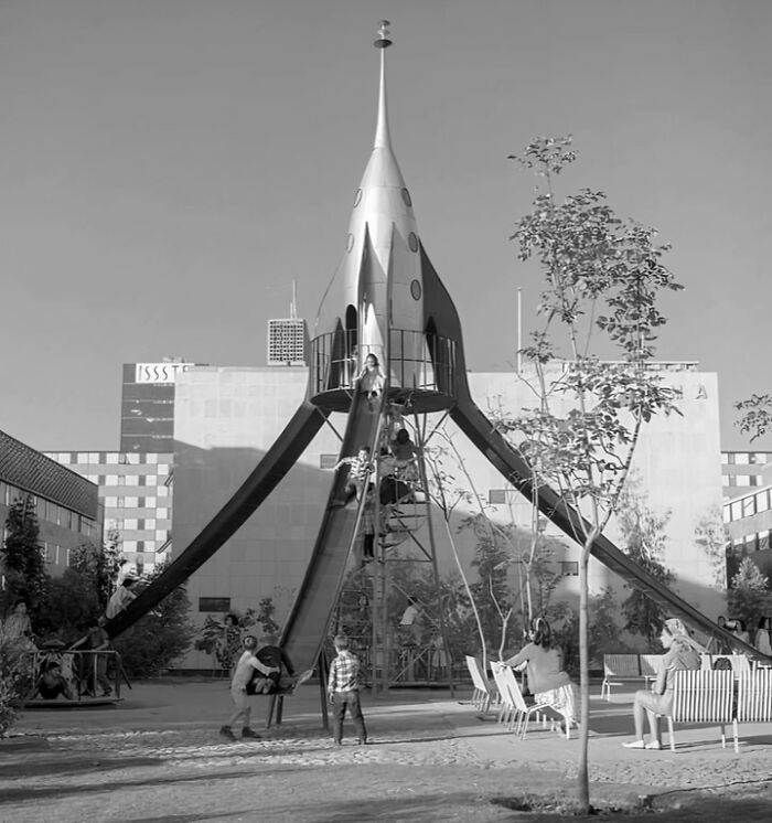 Historic playground with a rocket-shaped slide where children are climbing and playing outdoors in a retro urban setting.