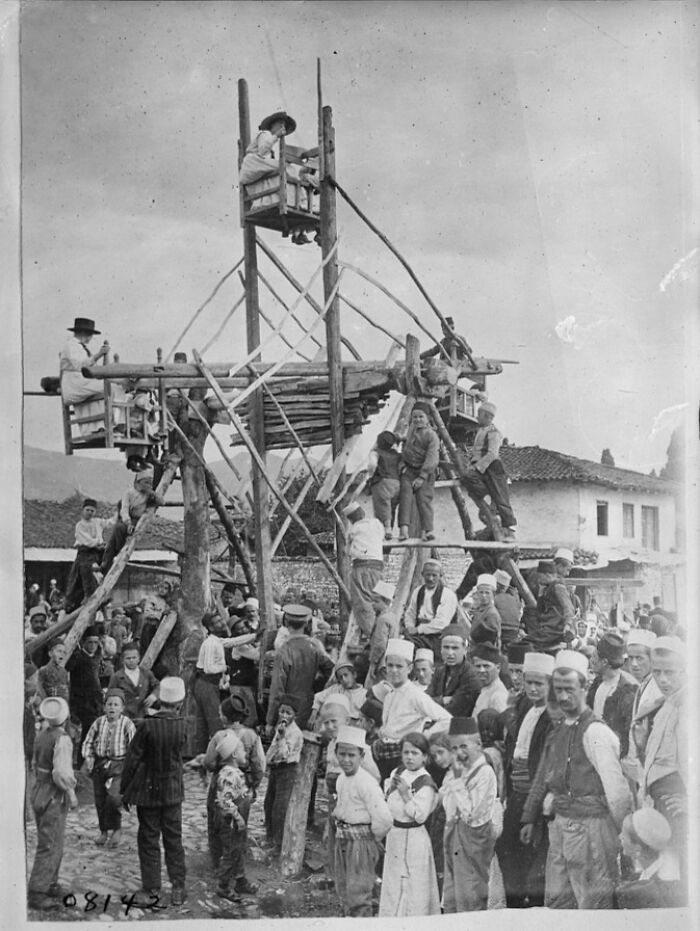 Historic photo of a playground with children and adults gathered around a wooden structure showing risky play from the past.