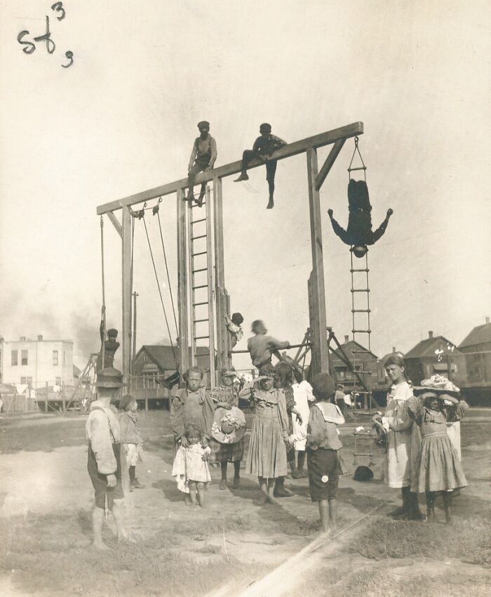 Historic playground scene with children playing on tall wooden structures, highlighting risky play from the past.