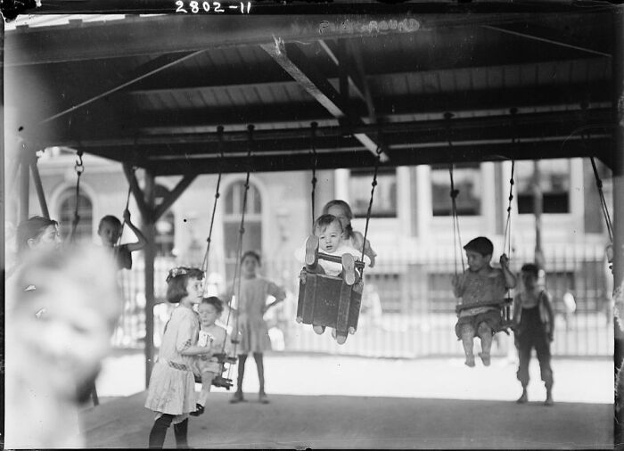 Historic photo of children playing on a playground swing set, showcasing risky childhood play activities from the past.