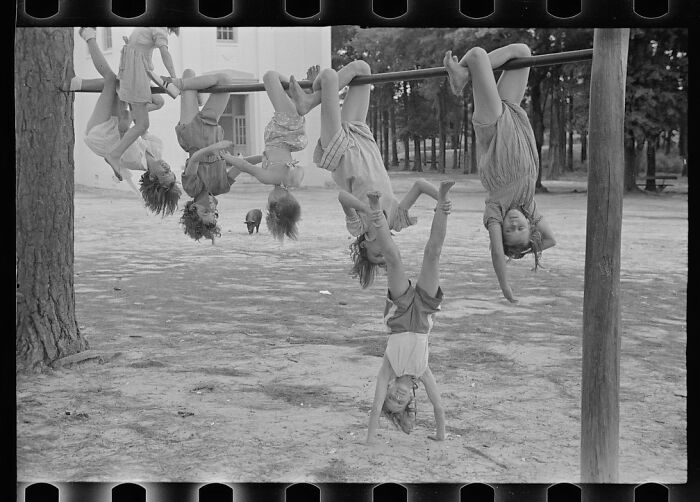 Historic black and white photo of kids playing dangerously on playground equipment hanging upside down and doing handstands.