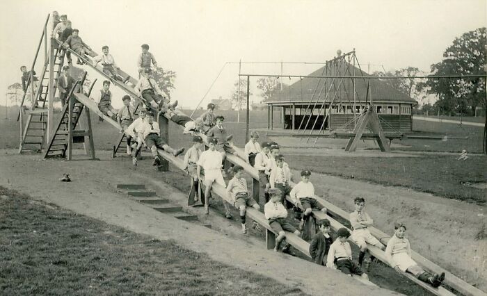 Historic playground photo showing children on a large wooden slide, highlighting risky play equipment from the past.