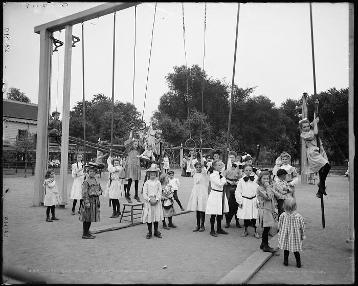 Historic playground photo shows children playing on risky vintage equipment in early 1900s outdoor setting.