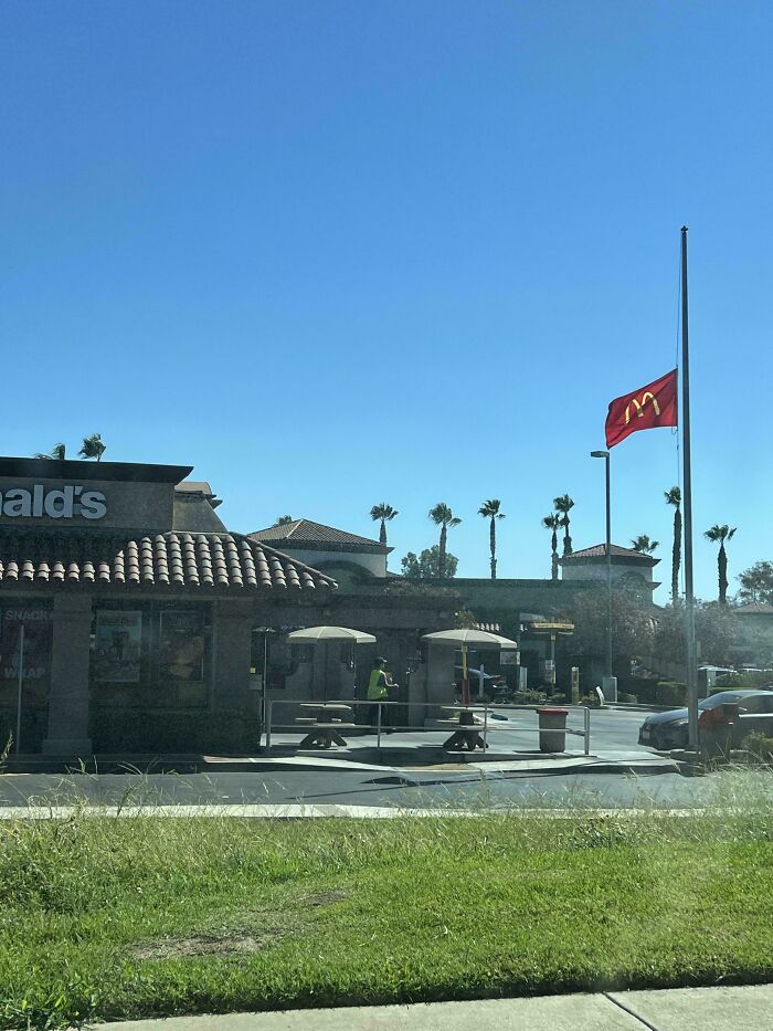 McDonald's flag flying at half-mast outside restaurant on a clear sunny day, showing moderately interesting scene.